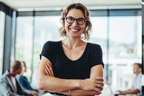 A young professional smiles and there are colleagues in the background