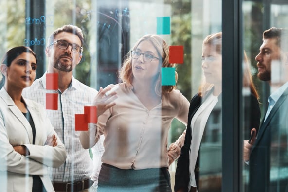 A group of co-workers in an office in conversation around a white board with sticky notes