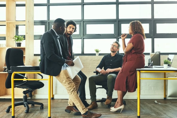 A group of sharply dressed professionals in conversation in a hip office space