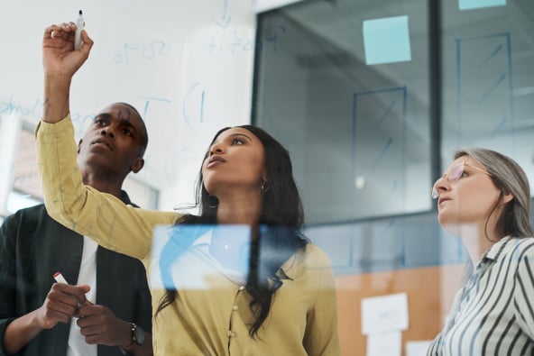 A group of colleagues collaborate on a see-through glass work board