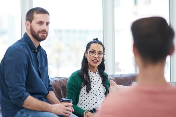 A group of professionals in conversation seated on couches in a sunny room