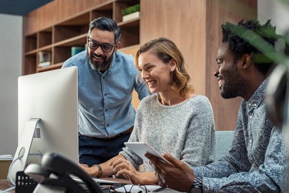 Three colleagues at work collaborate joyfully around a desktop monitor