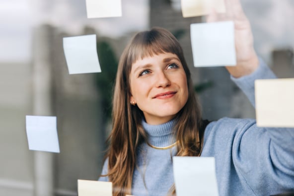 A person smiling places sticky notes on a clear glass wall 